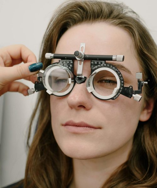 Crop oculist correcting phoropter on eyes of patient while selecting proper lens diopter during appointment in professional clinic